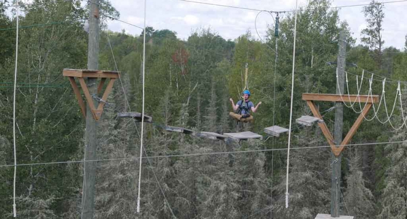 an outward bound student sits cross-legged while being suspended mid-air during a ropes course